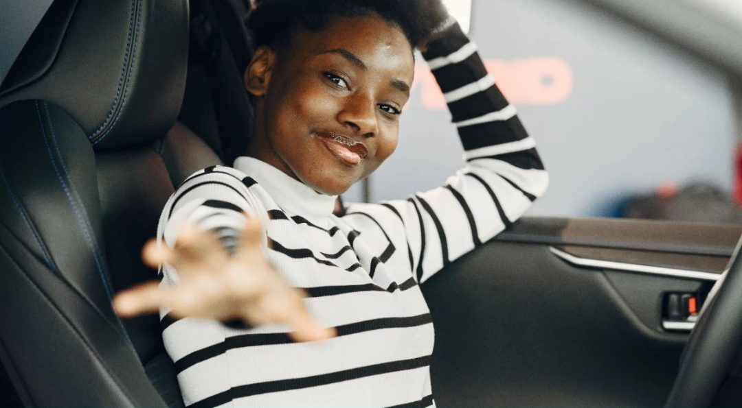 A passenger in the front seat, smiling and reaching a hand out to the camera